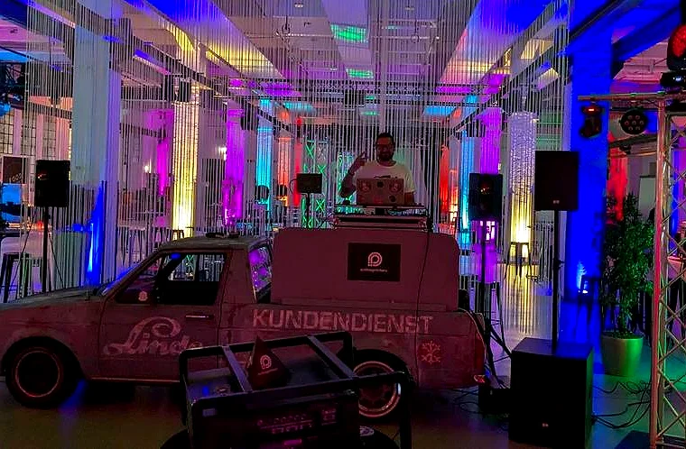 Eventhalle mit buntem Licht, in der Mitte der DJ-Caddy mit DJ
