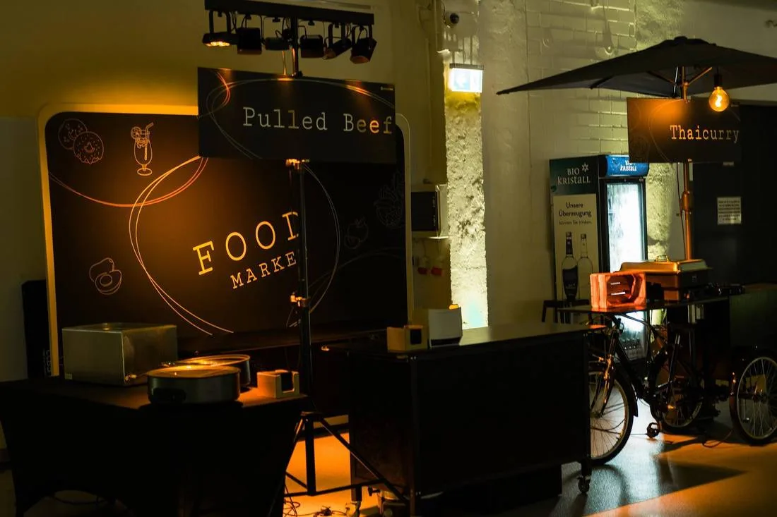 Food-Stationen in einer dunklen Halle, beleuchtetes Schild „Food Market“