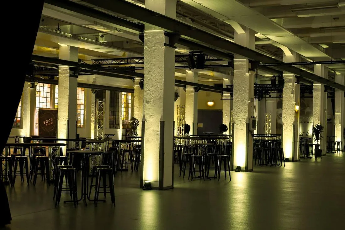 Große Industriehalle mit Säulen, Stehtischen und warmem Licht