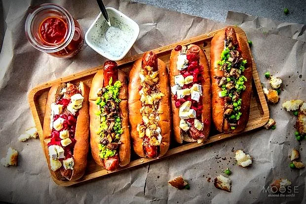 Fünf Hot Dogs mit bunten Toppings auf einem Holzbrett